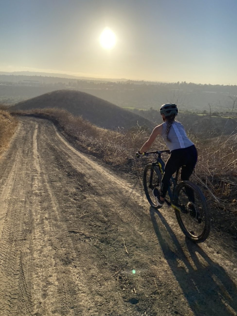 Rider on a hardtail mountain bike climbing a dirt road into the sunset